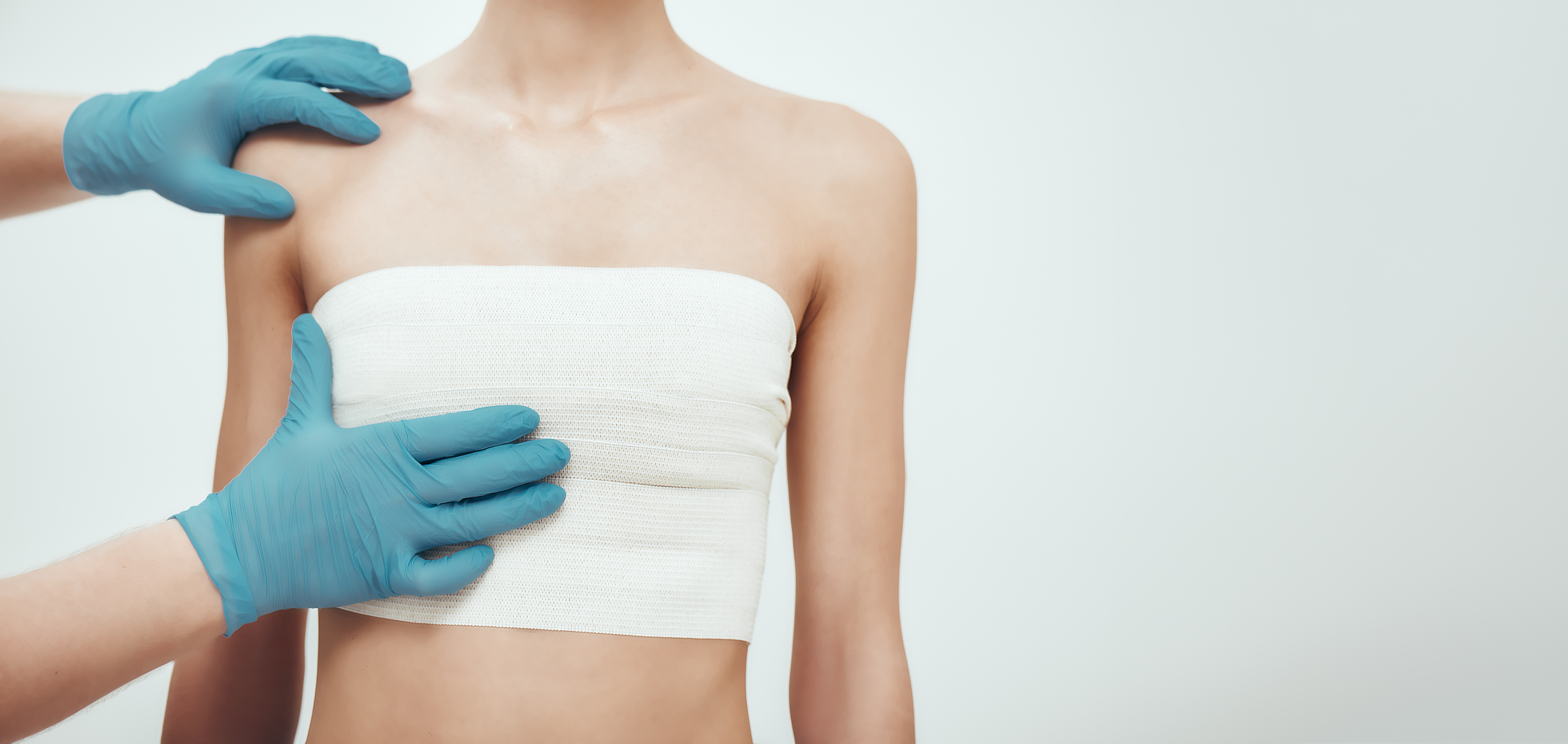 woman waiting for plastic surgery while surgeons in blue medical gloves measuring her breast